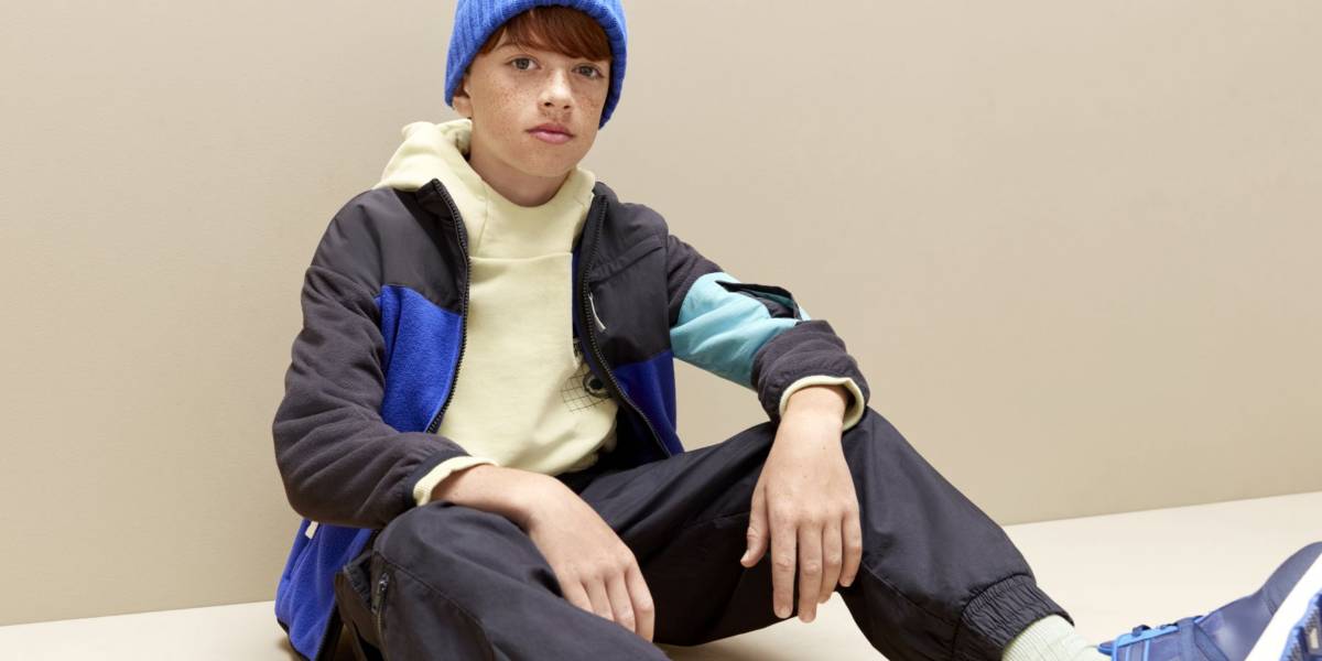 Boy wearing grey and blue tracksuit, cream hoodie and blue hat and shoes 
